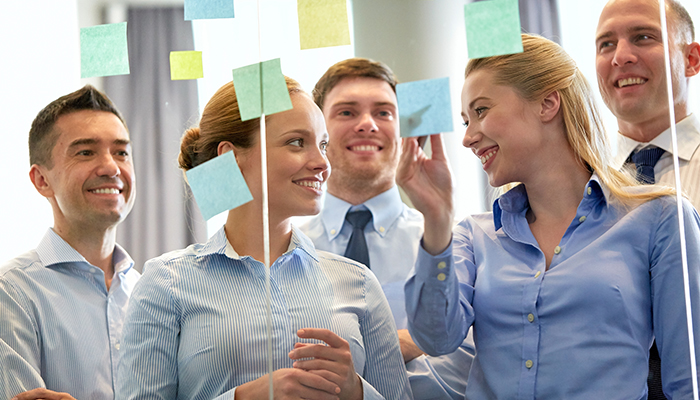 Mehrere Personen stehen vor Glasswand mit Post-its und koordinieren die Zusammenarbeit von Personaldienstleistern