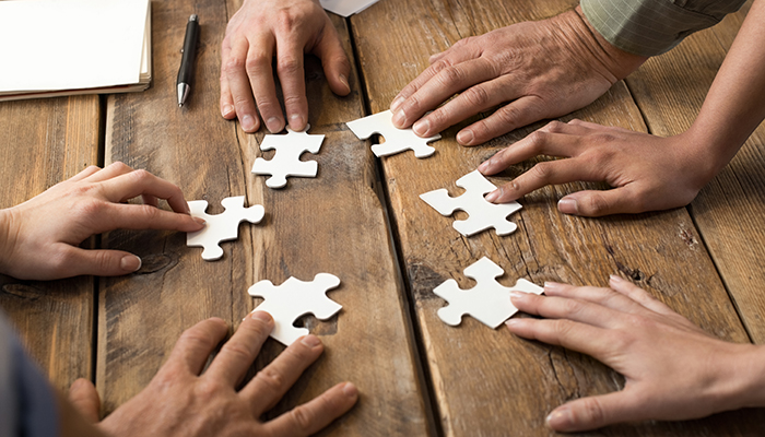 Symbolbild für Zusammenarbeit mehrerer Personaldienstleister: Menschen fügen auf einem Tisch Puzzleteile zusammen.